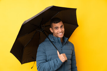 Young handsome man holding an umbrella over isolated yellow background with happy expression