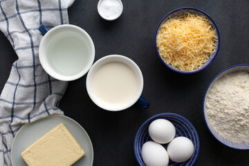 Ingredients for Traditional French Gougeres - savory cheese pastry flour, eggs, butter, milk, water, cheese and salt. Flat lay on dark grey background