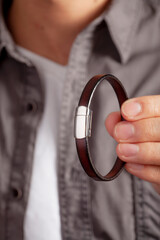 Brown leather men's bracelet, man in gray shirt wears brown bracelet with white stone in the middle on his left arm.