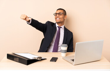 Young business man in his office with a laptop and other documents giving a thumbs up gesture