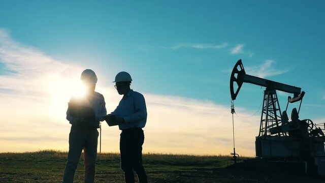 Two oil workers talking in an oil field at bright sunset