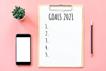 2021 New year concept. Goals list in stationery, blank clipboard, smartphone, pot plant on pink pastel color with copy space