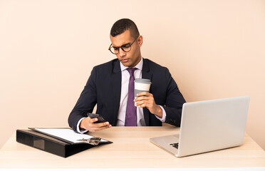 Young business man in his office with a laptop and other documents holding coffee to take away and a mobile