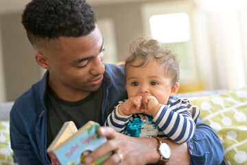 young african-american man reading book story to baby girl - 396300840