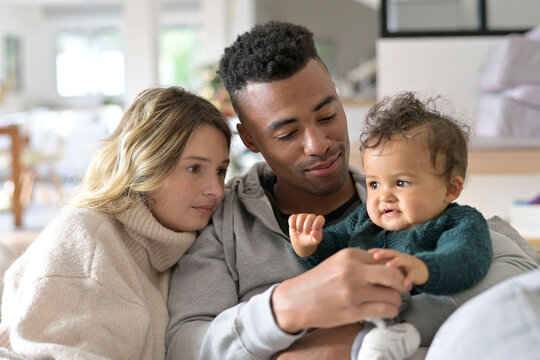 Young mixed-raced family at home cuddling baby girl