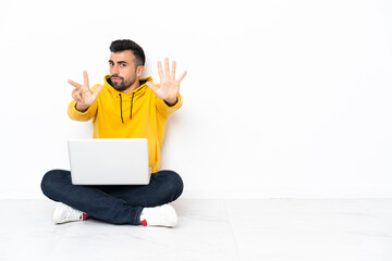 Caucasian man sitting on the floor with his laptop counting eight with fingers