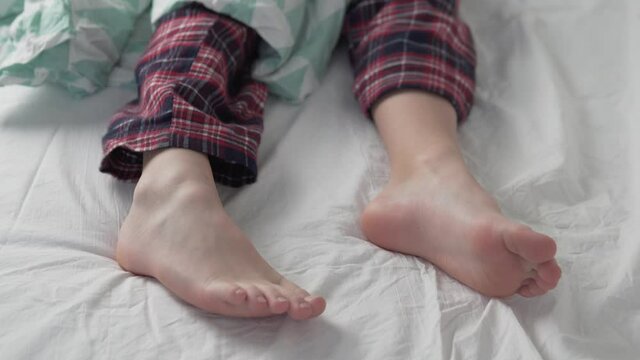 A boy in cool pants wakes up in the morning in a bed, close-up of the child's legs.
