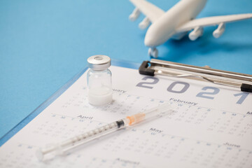 Vaccine with syringe, calendar 2021, and white plane, blue background