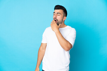 Caucasian man over isolated blue background yawning and covering wide open mouth with hand