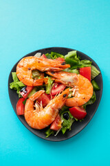 salad with fried shrimps on dark plate on blue background