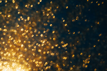 Gold glitter on dark blue bokeh abstract light defocused background.