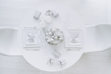 Diner Table for Celebrate X-mas Holiday Top View. Restaurant or Domestic White Desk Decorated Gift Boxes and Balls Toys on Tray, Glasses And Candles, Bow on Plates for Romantic Christmas Dating