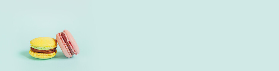 Sweet almond colorful pink yellow macaron or macaroon dessert cake isolated on trendy blue pastel background. French sweet cookie. Minimal food bakery concept. Flat lay top view, banner