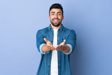 Caucasian man over isolated blue background holding copyspace imaginary on the palm to insert an ad