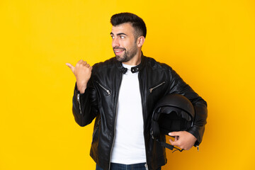 Caucasian man with a motorcycle helmet over isolated yellow background pointing to the side to present a product