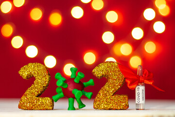 Golden glittering numbers 2021 with covid-19 virus and vaccine ampoule with bokeh on red background. Copy space.