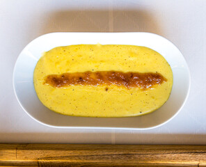 Mashed potatoes with black pepper, white pepper and nutmeg with gravy on top on a white tablecloth and red table runner, top view