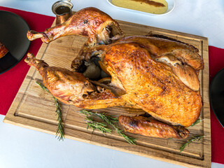 Christmas dinner table concept of whole roast turkey on wooden cutting board with mashed potatoes, glazed ham, gravy on white tablecloth and red table runner