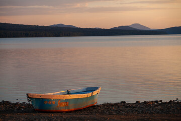 Obraz na płótnie Canvas Wooden boat on the pebble shore of a mountain lake against the backdrop of a beautiful sunset