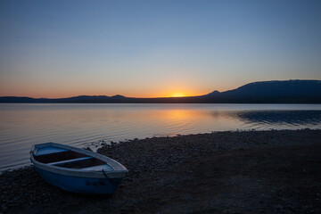 Fototapeta na wymiar Wooden boat on the pebble shore of a mountain lake against the backdrop of a beautiful sunset