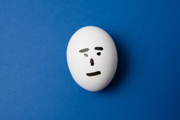Egg with an indifferent face, on blue background with copy space.
