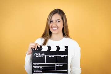 Young caucasian woman over isolated yellow background holding clapperboard very happy having fun