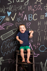 a small child of European appearance sits on a stool near a slate wall with drawings. boy draws with a smile. home leisure
