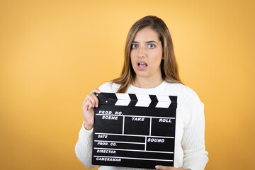 Young caucasian woman over isolated yellow background holding clapperboard very happy having fun