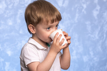 little boy drinks water from a disposable cup of cornstarch. ecologicaly clean. replacing plastic with modern biodegradable materials. child of European appearance close up