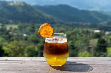 Black coffee orange mixed juice in glass with mountains view
