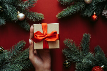 Woman hands holding gift box. Fir tree and holiday decorations. New Year holiday concept. Flat lay, top view. Merry christmas card