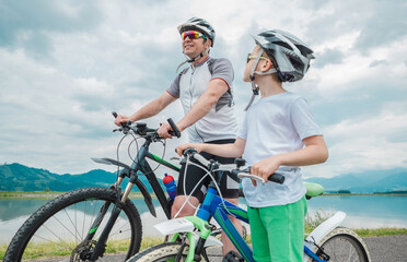 Obraz premium Father and son ride, cycling their bikes together, on sunny day, Happy family in helmets is riding bikes having fun.