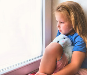 Stay at home. Quarantine coronavirus pandemic prevention. sad child girl sitting on windowsill and looks out window want to walking. Covid 19. Abstract white window with place for text