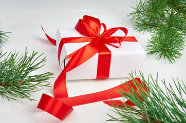 Christmas gift box with red ribbon and pine tree branches on white wooden background