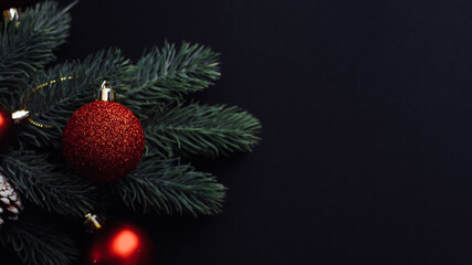 Christmas tree branch with red Christmas balls on a black background. Xmas greeting card with space. Flat lay, top view