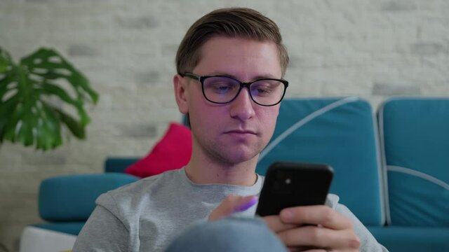 Young man sits on bean bag and urf the internet using a mobile phone, staying isolated at home. Having fun.