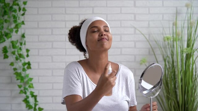 Young woman with eyes closed spraying facial mist at home