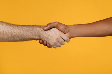 Close up cropped photo of young two friends european african american men holding hands folded isolated on bright yellow colour wall background studio portrait.