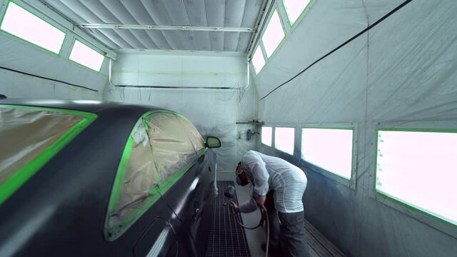 Car body painter spraying car in paint booth