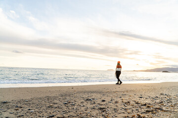 chica con gorro rojo y jersey de lana caminando andando en la arena de la playa mirando observando...