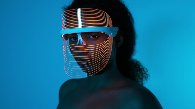 Woman wearing blue light therapy mask against blue wall