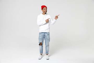 Full length of funny cheerful young african american man 20s years old in casual streetwear hoodie pointing index finger aside on mock up copy space isolated on white background, studio portrait.