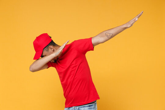 Delivery employee african man in red cap blank tshirt uniform workwear work courier service on coronavirus covid-19 virus concept doing dab hip hop dance hands gesture isolated on yellow background.