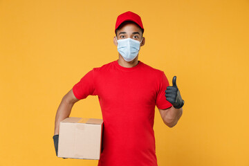 Fototapeta na wymiar Delivery employee african man in red cap blank print t-shirt face mask gloves uniform work courier service on quarantine covid-19 virus concept hold cardboard box isolated on yellow background studio.