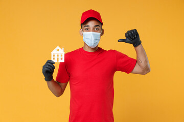 Delivery employee african man in red cap print t-shirt face mask gloves uniform work courier service to home on quarantine coronavirus covid-19 virus concept hold house isolated on yellow background.