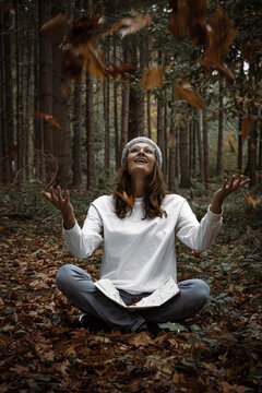 Lady throwing leaves up sitting in the forest