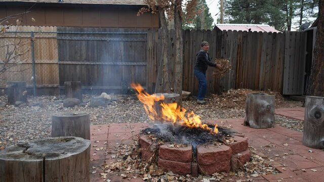 A Woman Burning Leaves In Her Back Yard In Autumn