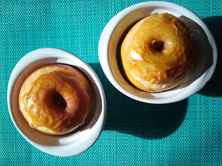 Two freshly baked apples in white bowls on blue background. Healthy snack concept. Top view. Hard light.