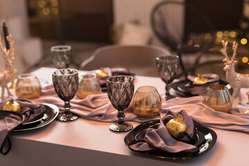 Close up of festive Christmas table setting with empty wine glasses and black plate with gold garnet