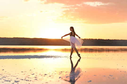 Tender girl young ballerina in a pink transparent skirt on the lake at sunset.